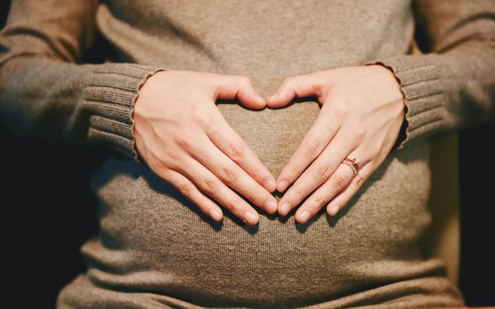 Hands making a heart shape on a pregnant belly